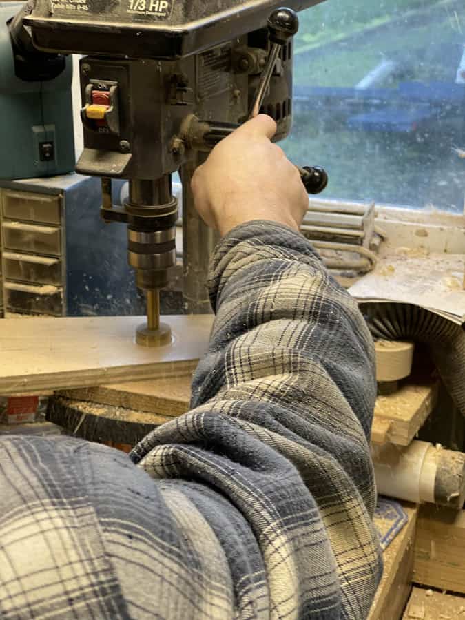 Using a drill press and forstner bit to drill the holes for the pool cues into the shelves